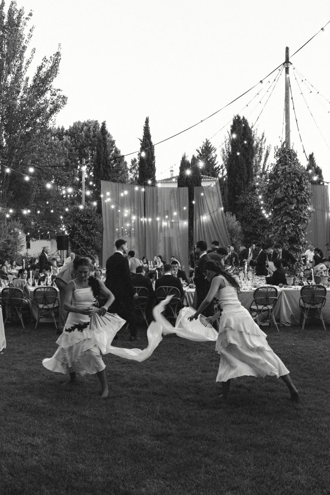 Dos bailaoras con abanicos y velos entre las mesas de un banquete de boda en un jardín
